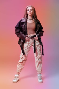 Göz kamaştırıcı rock tarzı. Siyah deri ceketli, beyaz spor pantolonlu ve spor ayakkabılı pembe stüdyo arka planında gür uzun saçlı modern bir genç kız. Gençlik modası. 