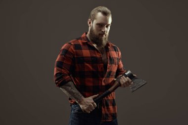 Elinde balta tutan ekose gömlekli vahşi sakallı bir adamın portresi. Koyu gri stüdyo geçmişi. Erkek güzelliği ve erkeklik.