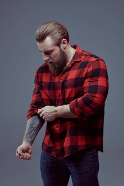 Berber dükkanı reklamı. Gri bir stüdyo arka planında ekose gömlekli, sakallı yakışıklı bir adamın portresi. Erkek güzeli. Erkeklik ve güç.