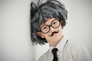 Küçük Bilim Adamı. Gözlüklü, bıyıklı ve peruklu komik çocuk. Sanki bir profesör kameraya yorgun bakıyor. Kopya alanı olan beyaz stüdyo arkaplanı. Eğitim ve erken kalkınma.