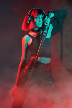 Uzay teknolojisi. Sanal gerçeklik oyunları. Elinde kılıçla tetikte bekleyen militan bir siber kızın portresi. Neon kırmızısı mavi ışıklandırma.