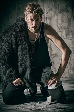 Siyah kürklü zalim bir adam dizlerinin üstüne çöküp şeytani bir bakışla silah ve para tutuyor. Suç dünyası, paranın gücü. Yeşil ışık.