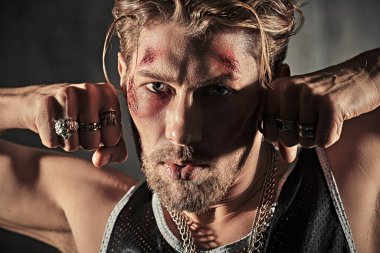 Kötü adam konsepti. Aksiyon filmi kahramanı. Yüzünde morluklar ve yaralar olan sert bir erkek haydut, karanlık bir odada duruyor ve saldırganca bakıyor..