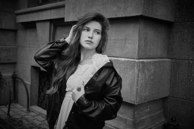 Şehir caddesinde duran uzun saçlı güzel romantik bir kızın siyah beyaz portresi. İnsanlar, duygular. Şehir yaşam tarzı.