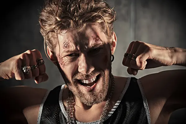 Yüzünde çizikler ve yaralar olan, beton duvarlarla karanlık dumanlı bir odada duran ve kameraya saldırganca bakan vahşi bir adamın portresi. Aksiyon filmi kahramanı. Dedektif filmi. Kötü adam..