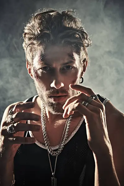 Aksiyon filmi kahramanı. Yüzünde çizikler ve yaralar olan sert bir adamın portresi, karanlık dumanlı bir odada beton duvarlarla duruyor ve bıkkın bir şekilde kameraya bakıyor. Dedektif filmi. Kötü adam..