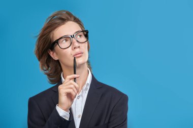 Takım elbiseli ve gözlüklü bir liseli çocuk düşüncelerinde. Stüdyo mavi arkaplan ve metin için boşluk. Eğitim.