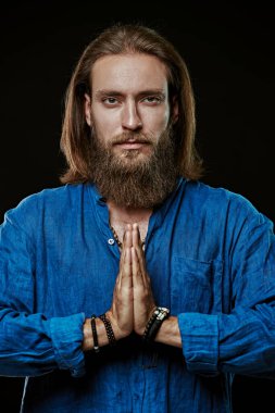 Sakallı, orta boylu, doğal pamuk mavisi gömlekli bir adam siyah bir stüdyo geçmişi için dua ediyor. Din.