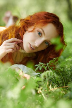 Beyaz bir gecelik giymiş, parlak kırmızı dalgalı saçlı güzel bir kız çayırdaki çimlere uzanıyor ve tatlı tatlı gülümsüyor. Romanın kadın kahramanı. Romantizm çağı, 18-19 yüzyıl..