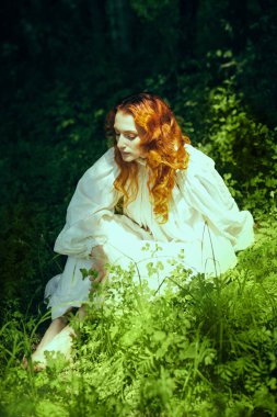 18-19 yüzyıl. Güzel, dalgalı, kızıl saçlı, uzun beyaz gömlekli romantik bir kız güneşli bir yaz gününde parkta dinleniyor. Romantizm çağı..