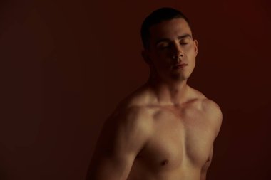 Atletik yapılı yakışıklı bir gencin koyu renk bir anahtarındaki resim. Fotokopi uzayı olan siyah bir arkaplanda stüdyo çekimi. Erkek güzeli..