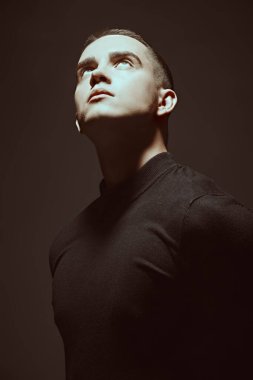 Duygular ve ruh hali. Siyah elbiseli genç bir adamın sanat portresi. Karanlıkta duran ve yüzünü aydınlatan bir ışık huzmesi. Siyah stüdyo geçmişi. Erkeklerin psikolojisi.