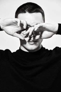 Duygular, duygular. Kısa saçlı, siyah elbiseli ve yüzünü elleriyle örten yakışıklı bir gencin sanat portresi. Siyah beyaz portre. Bir adamın psikolojisi..