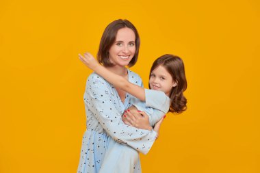 Küçük bir kız sevgili annesiyle neşeyle oynar. Mutlu bir aile. Sarı arka planda stüdyo resmi.