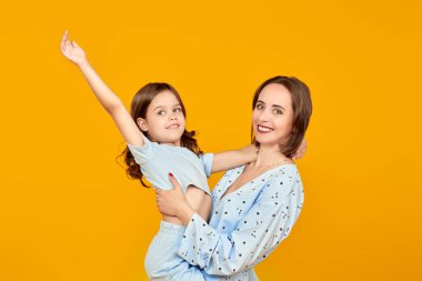 Küçük bir kız sevgili annesiyle neşeyle oynar. Mutlu bir aile. Sarı arka planda stüdyo resmi.