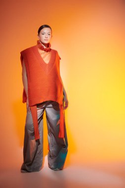 Tasarımcı örgüsü. Geniş paçalı pantolonla poz veren şık bir manken stüdyoda karışık renkli ışıkta örülmüş bir panço. Parlak renkler. Yeni moda yarı sezon koleksiyonu. 