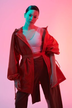 Yaz koleksiyonu. Tarz sahibi turuncu ceketli ve geniş bacaklı kahverengi pantolonlu bir manken kız. Karmaşık renk ışıklandırmasında pembe bir arkaplan karşısındaki stüdyo çekimi. 