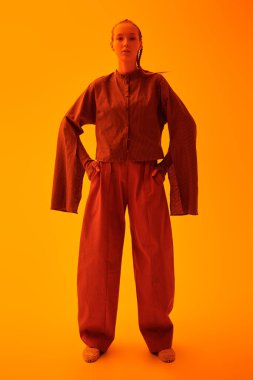 Özel tasarım koleksiyonu. Tasarımcı kahverengi deri ceket, bluz ve turuncu geniş bacak pantolonuyla poz veren güzel bir manken kız. Stüdyo görüntüsü gri arka planda. Şık güneş gözlükleri. Eğilimler.