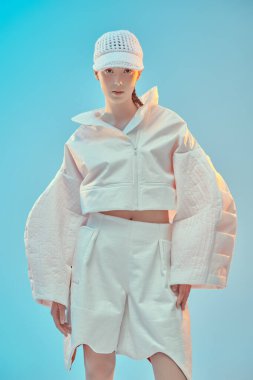 Beyaz ceketli, beyaz pantolonlu ve mavi şapkalı güzel bir model. Gelecekçi tarzı. Yüksek moda.