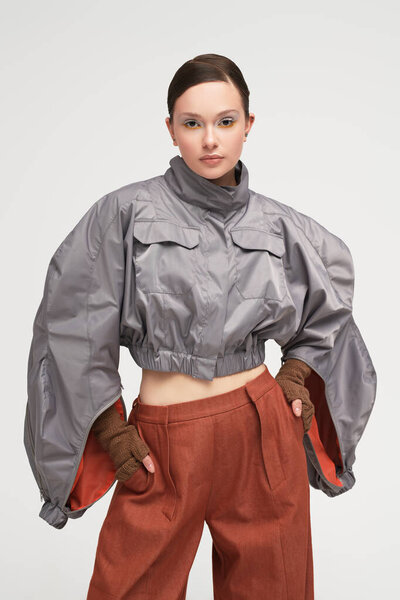 Портрет красивой девушки-модели, позирующей в стильной серой куртке и широких коричневых брюках на белом фоне студии. Футуристический стиль моды. Высокая мода.