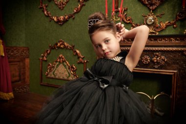 Kabarık siyah bir gece elbisesi ve lüks bir iç mekanda pahalı bir inci kolye giyen güzel bir kız model. İyi akşamlar çocuklar. Giysiler ve mücevherler. Akşam saç stilleri.