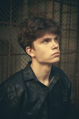 Siyah elbiseli modern genç bir adam büyük bir şehrin karanlık bir sokağında metal bir ızgaranın karşısında duruyor. Kentsel yaşam tarzı.