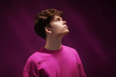 Mor bir arka planda, kırmızı bir kazakla fotokopi çeken modern bir mankenin portresi. Gençlik modası. Erkek saç stili. Karışık ışık.