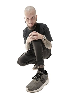 Punk rock müziği. Gayri resmi görünüşlü, kafası kazınmış, dudağında ve kulaklarında piercing olan, vücudunda dövmesi olan bir adam stüdyoda siyah giysiler içinde poz veriyor. Beyaz stüdyo geçmişi.