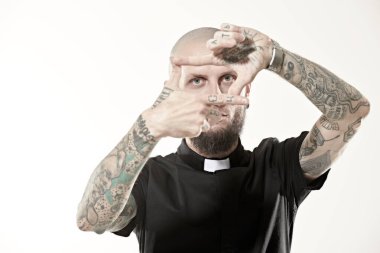 Gayri resmi bir görünüşü olan, kafası tıraşlı, kulaklarında ve dudaklarında piercingler olan, vücudunda dövmesi olan bir adam parmaklarıyla kameraya dalgın dalgın bakıyor. Beyaz stüdyo geçmişi.