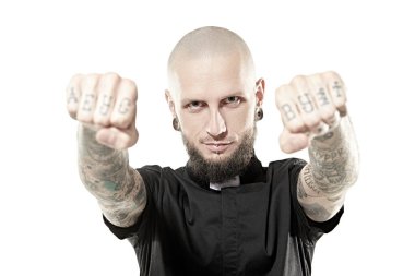 Tıraş olmuş, siyah bir papaz gömleği giymiş zalim bir adam yumruklarını dövmeyle gösteriyor. Antisosyal davranış, protesto ifadesi. Beyaz stüdyo geçmişi.