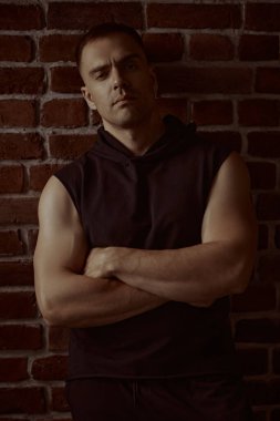 Erkekler, erkeklik ve güç. Siyah kapüşonlu güçlü bir adamın portresi, odaklanmış ve yoğun bir şekilde kameraya bakıyor. Arka planda tuğla duvar var. Halk konsepti.