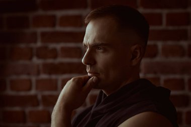 Erkekler, erkeklik ve güç. Siyah kapüşonlu güçlü bir adamın yakın plan portresi. Odaklanmış ve düşünceli bir şekilde ileriye bakıyor. Arka planda tuğla duvar var. Halk konsepti. 