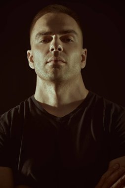 Yakışıklı kaslı bir adam sakince kameraya bakar. Siyah arka planda stüdyo portresi. İnsanlar ve duygular. Erkekler ve erkeklik. Spor..