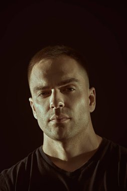 İnsanlar ve duygular. Yakışıklı kaslı bir adam sakince kameraya bakar. Siyah arkaplanda fotokopi alanı olan bir stüdyo resmi. Yaşam tarzı, seçimler. Spor..