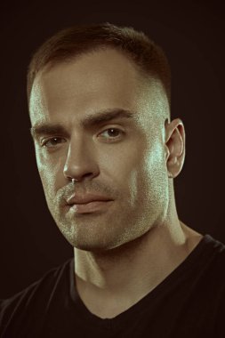 Erkekler, erkeklik ve güç. Siyah bir stüdyo arka planında siyah tişörtlü yakışıklı ve güçlü bir adamın yakın plan portresi. Halk konsepti. 