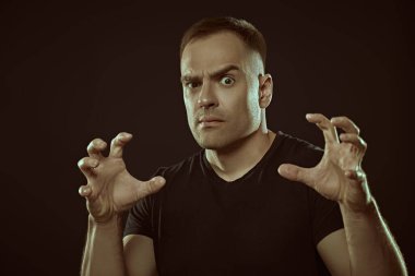 Agresif bir adam açıkça kameraya bakar ve ellerini ileri uzatır. Siyah arka planda stüdyo portresi. İnsanlar ve duygular.