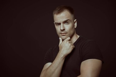 Güçlü, kendine güvenen, atletik yapılı bir adam. Siyah arkaplanda fotokopi alanı olan bir stüdyo resmi. Güç sporları, sağlık ve aktif yaşam konumu.