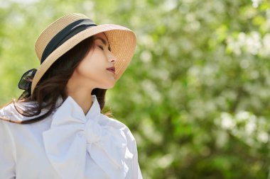 Yaz tatili. Güzel bir Asyalı genç kadın yemyeşil bir arka planda bir yaz parkının arka sokağında yürüyor. Mutlu güneşli günler..