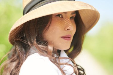 Güzel bir Asyalı genç kadın yemyeşil bir arka planda bir yaz parkının arka sokağında yürüyor. Mutlu güneşli günler. Yaz tatili.