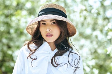 Beyaz bluz ve hasır şapkalı Asyalı romantik bir genç kadının portresi çiçek açan elma ağacının çiçeklerinin arasında duruyordu. Bahar çiçekleri ve güzellik.