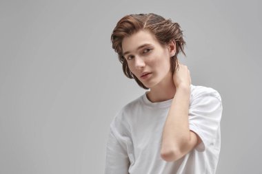 İnsanlar, duygular. Beyaz tişörtlü, kameraya bakan yakışıklı, düşünceli bir gencin portresi. Metin için yeri olan gri arkaplan. Okul, eğitim. Modern yaşam tarzı.