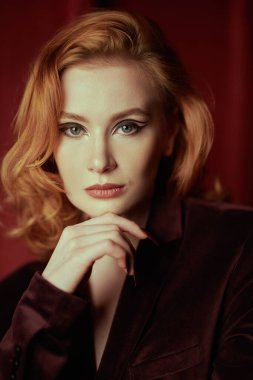 Okları ve saç stili olan zarif bir makyaj. Kadın güzelliği ve tarzı. Pahalı kadife ceketli, loş ışıklı bir odada kızıl saçlı çekici bir genç kadın. Moda ve kadınlık.