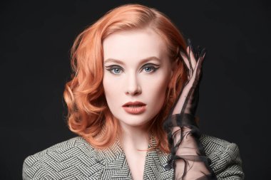 Siyah stüdyo arka planında ceketli, kızıl saçlı çekici bir kadının portresi. Zarif oklarla makyaj yapın. Hollywood dalgası saç stili. Zarif retro tarzı ve modası. 