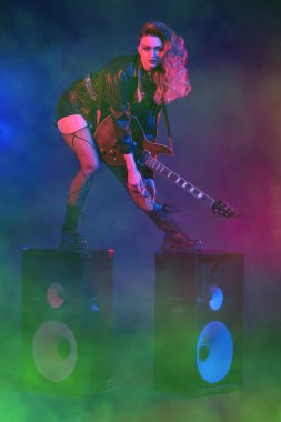 Parlak bir rock yıldızı müzisyen kız sahnede duruyor. Rock gitaristi, şarkıcı. Glam rock tarzı.