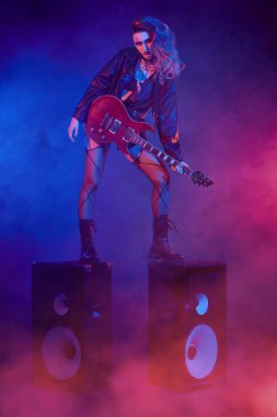 Glam rock tarzı. Parlak bir rock yıldızı müzisyen kız sahnede duruyor. Rock gitaristi, şarkıcı.