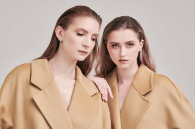 Uzun bej keçeli ceketlerle poz veren iki güzel model kızın portresi. Beyaz stüdyo geçmişi. Yarı sezon modası.