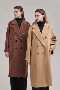 Yarı sezon kadın modası. Fiyakalı keçeli paltolarla poz veren iki model kızın tam boy portresi. Stüdyo beyaz arkaplan.