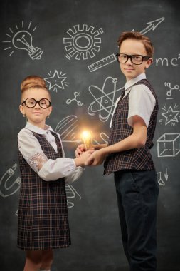 Sevimli okul çocukları siyah karatahta arka planında ampulle poz veriyorlar. Eğitim ve erken gelişim. Küçük Bilim adamları.