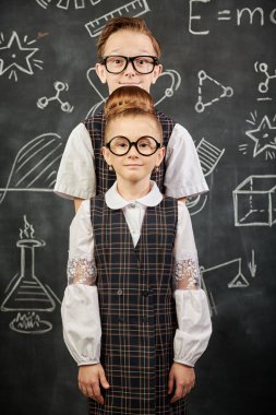 İki küçük tatlı okul çocuğu tahtaya poz veriyor. Eğitim ve erken gelişim. Küçük Bilim adamları. Siyah bir karatahtanın arka planı.