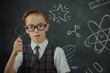 Okul üniformalı ve gözlüklü bir çocuğun kameraya ciddi ciddi baktığı bir fotoğraf. Bilimsel çizimleri olan siyah bir kara tahta. Eğitim. Genç bilim adamı.